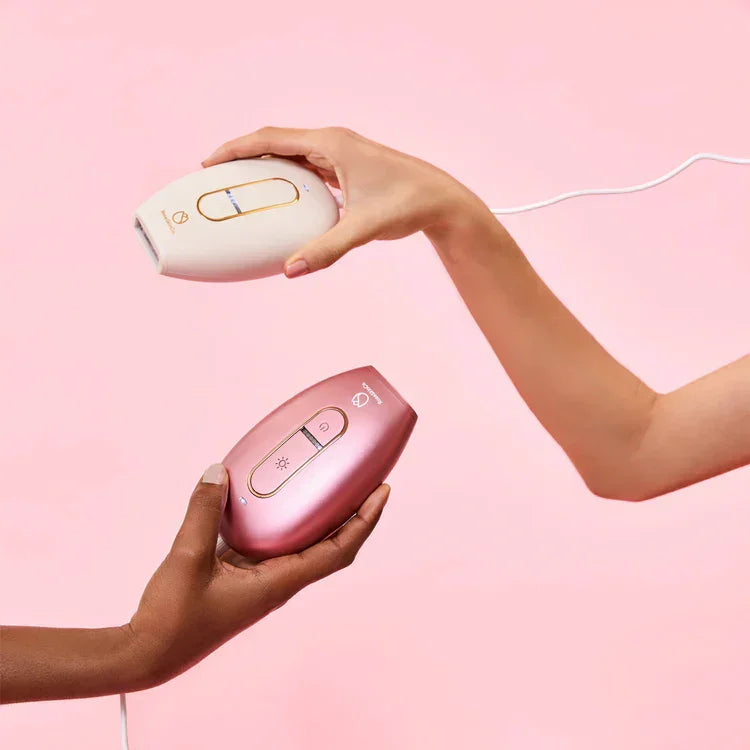 Two hands holding LaxeHaven rose and white hair removal devices against a pink background