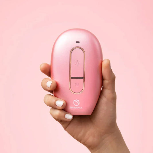 Hand holding RoseSkinCo Lumi IPL hair removal handset in rose gold, pink background, LaxeHaven